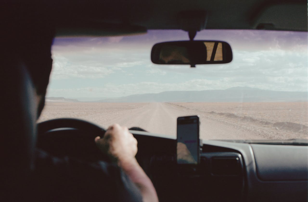 View from inside a car driving through a vast, empty desert landscape.