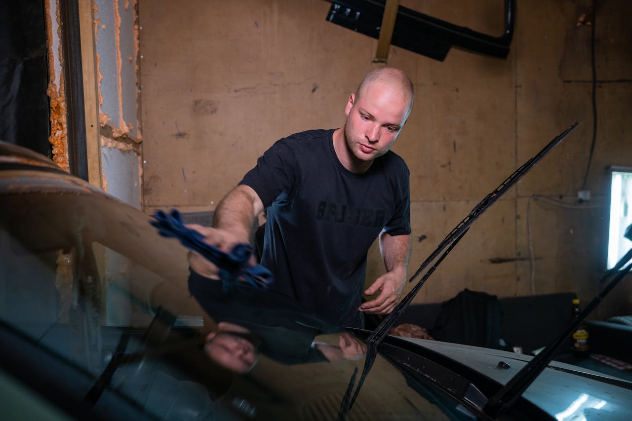 discover A man wipes a car windshield inside a garage, focused on cleaning.